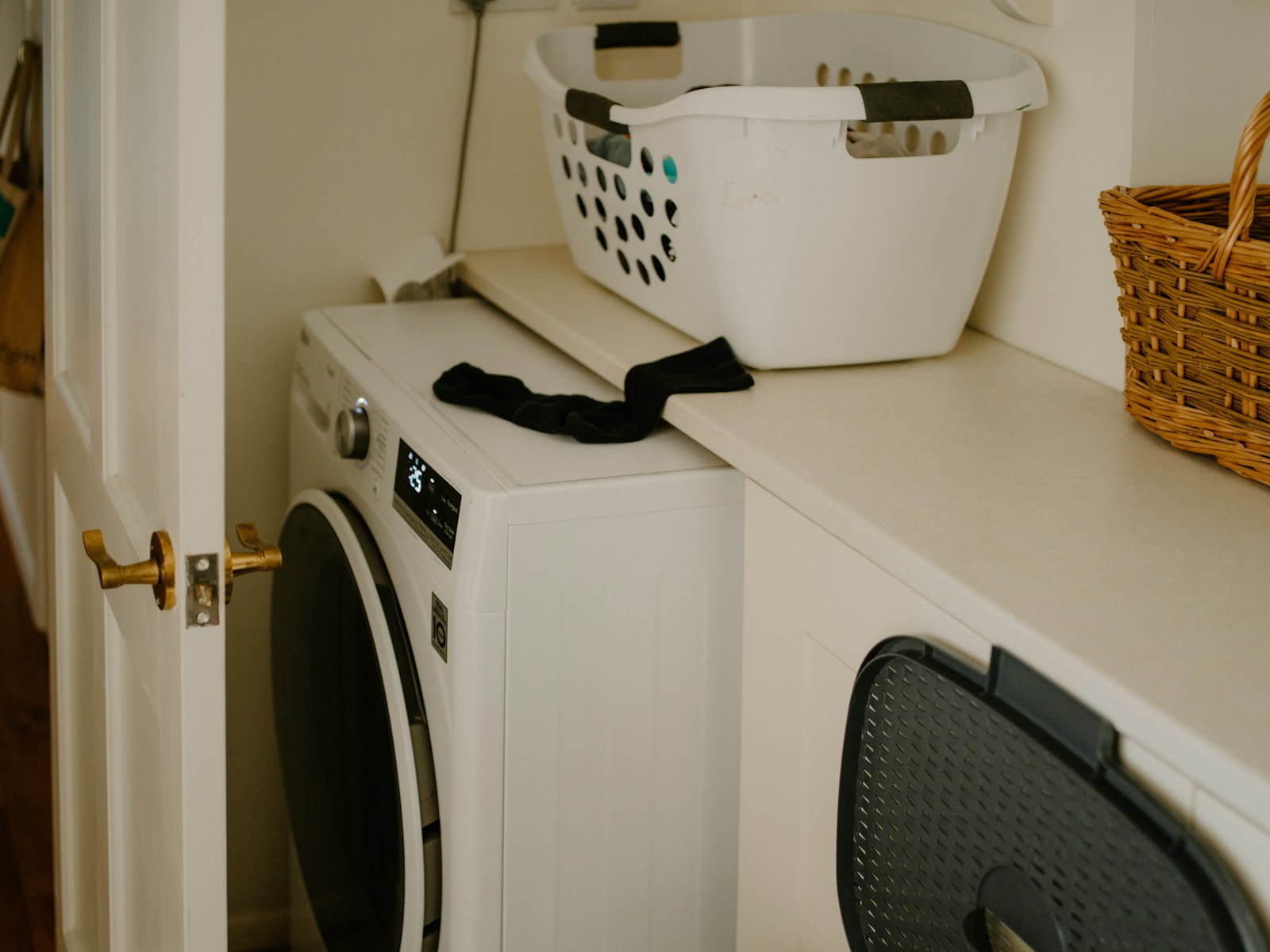 White front-load washing machine beside a laundry basket in a clean laundry area
