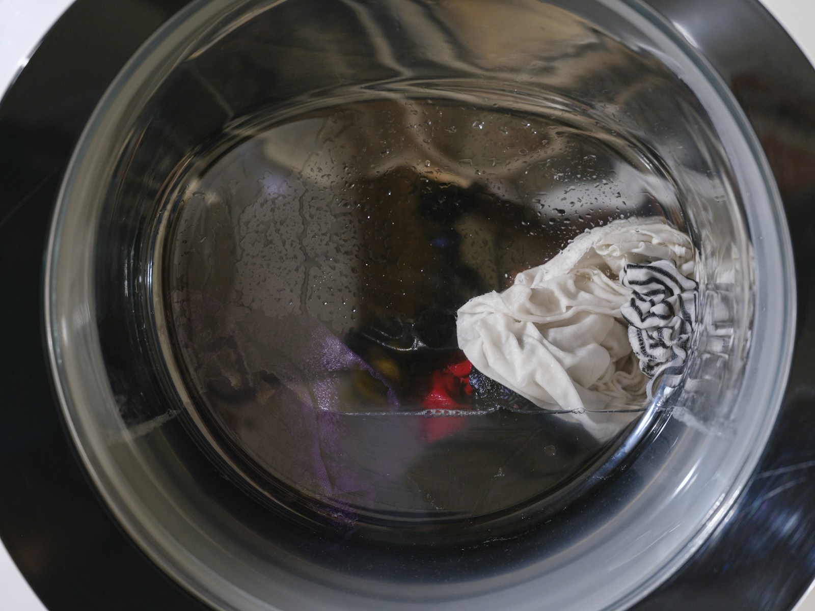 Washing machine drum with clothes and water visible through the door